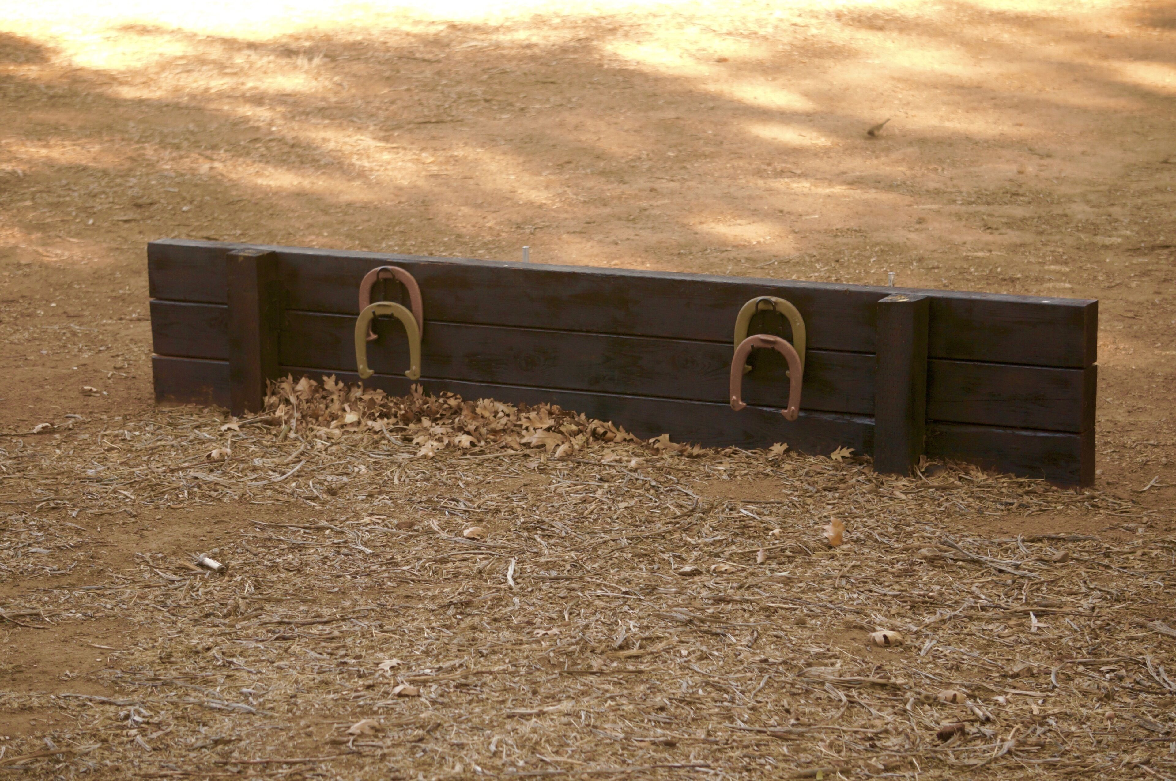 Un banc en bois, orné de motifs métalliques, est posé sur un sol recouvert de feuilles et de brindilles séchées.