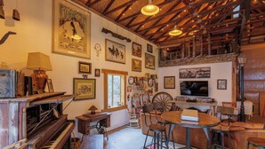 Una habitación acogedora con techo de madera, un piano, una mesa de comedor con sillas y varias fotografías enmarcadas en las paredes.