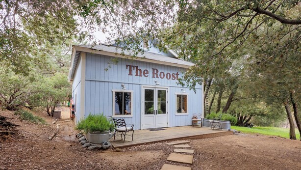 Un edificio rústico llamado "The Roost" con una terraza de madera, plantas en macetas y asientos al aire libre.