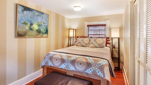 Quarto com cama, mesa de cabeceira, abajur, janela com persianas e um quadro na parede.