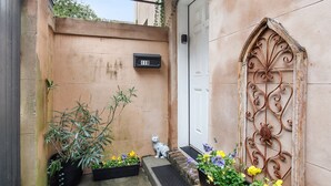 Uma entrada estreita com uma caixa de correio, um portão de ferro decorativo e plantas em vasos.