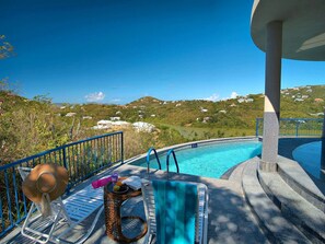 Zona de piscina con vistas a una colina, una silla de descanso, un parasol y una mesita con un sombrero y fruta.