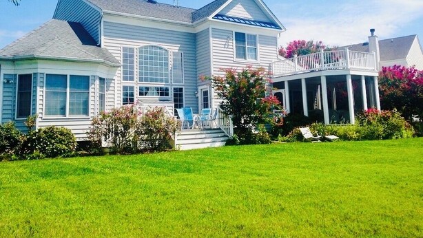 A two-story house with a porch, a covered front porch, and a well-maintained lawn. - Waterfront 5B+den Bethany Lakes, POOL,Pickleball,Gym, 5 min to beach, dogs ok (Bethany Beach)