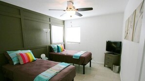 Ein Schlafzimmer mit zwei Betten, einem Deckenventilator, einem Fernseher und einem Fenster.