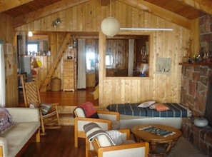 A cozy cabin interior with a wooden interior, a stone fireplace, and a staircase leading to another room.