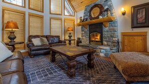 A cozy living room with a stone fireplace, leather furniture, and large windows. - The Stemwinder Chalet by Simply Kimberley (Kimberley)