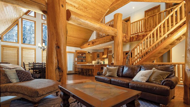 A spacious living area with a large wooden staircase, leather sofas, and a dining area with a high ceiling and large windows. - The Stemwinder Chalet by Simply Kimberley (Kimberley)
