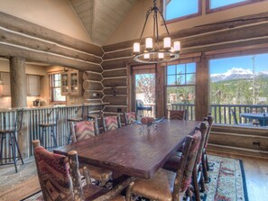 A rustic wooden dining room with a large table and chairs, a chandelier, and large windows offering mountain views. - Big Sky Vacation Rentals: PR Manitou 13 (Big Sky)