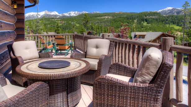 Terraza de madera con mobiliario de mimbre y vistas a montañas nevadas.