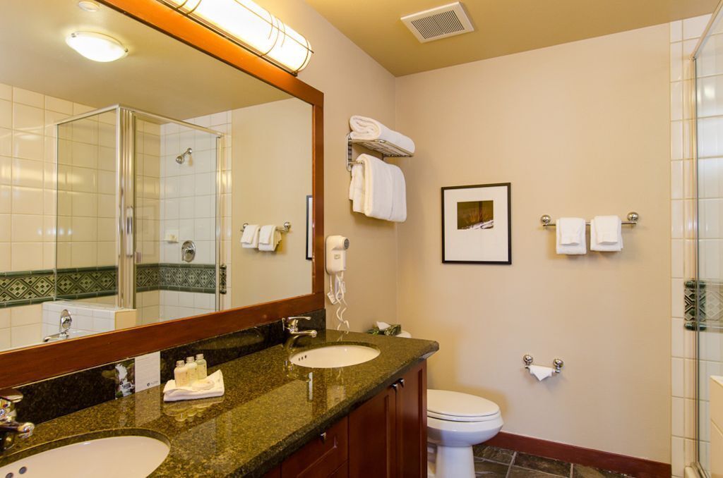 Un baño de hotel con dos lavamanos, un espejo grande, una ducha y un inodoro.