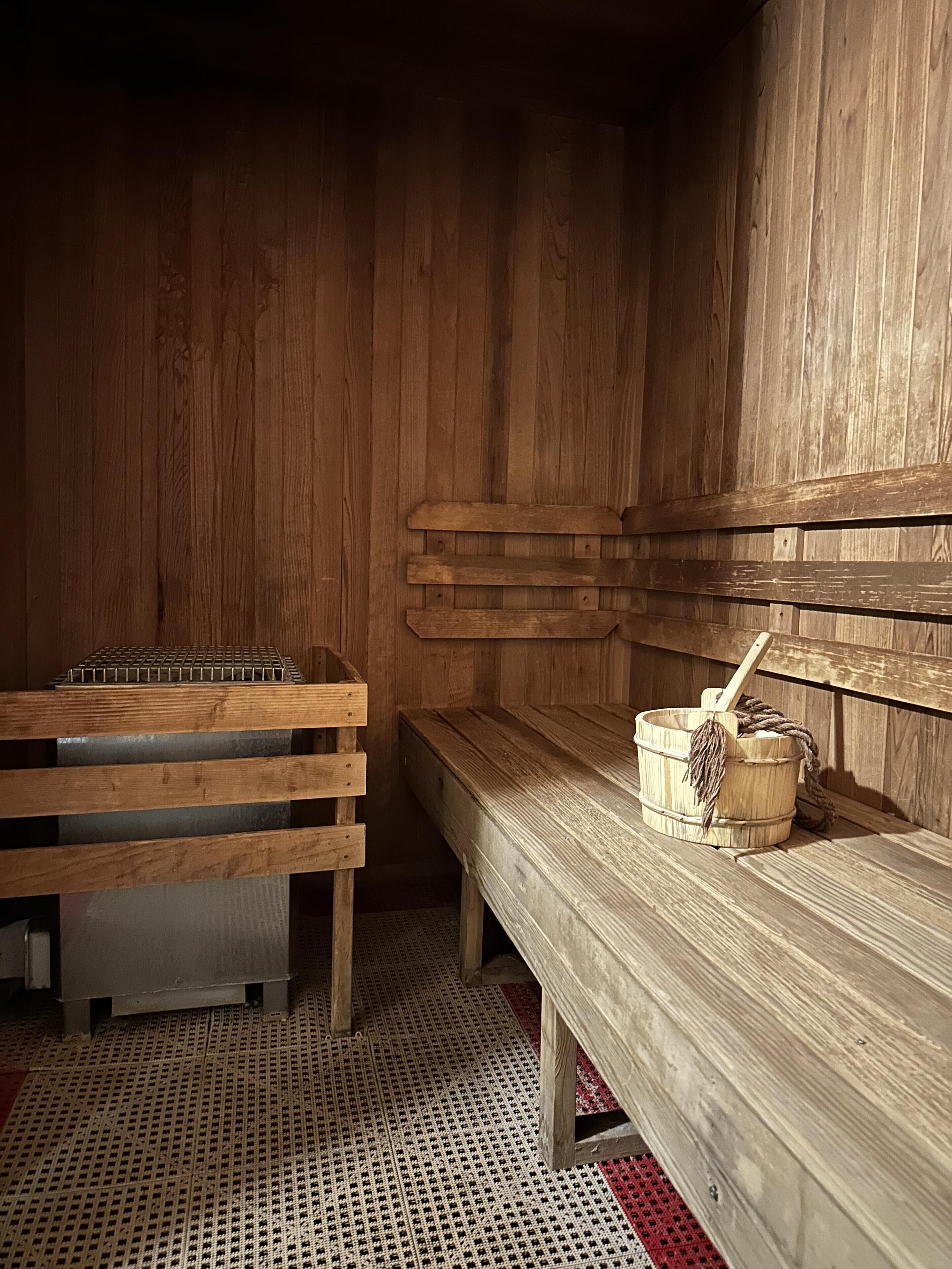 Un sauna en bois, avec des bancs et un seau en bois muni d’une brosse.
