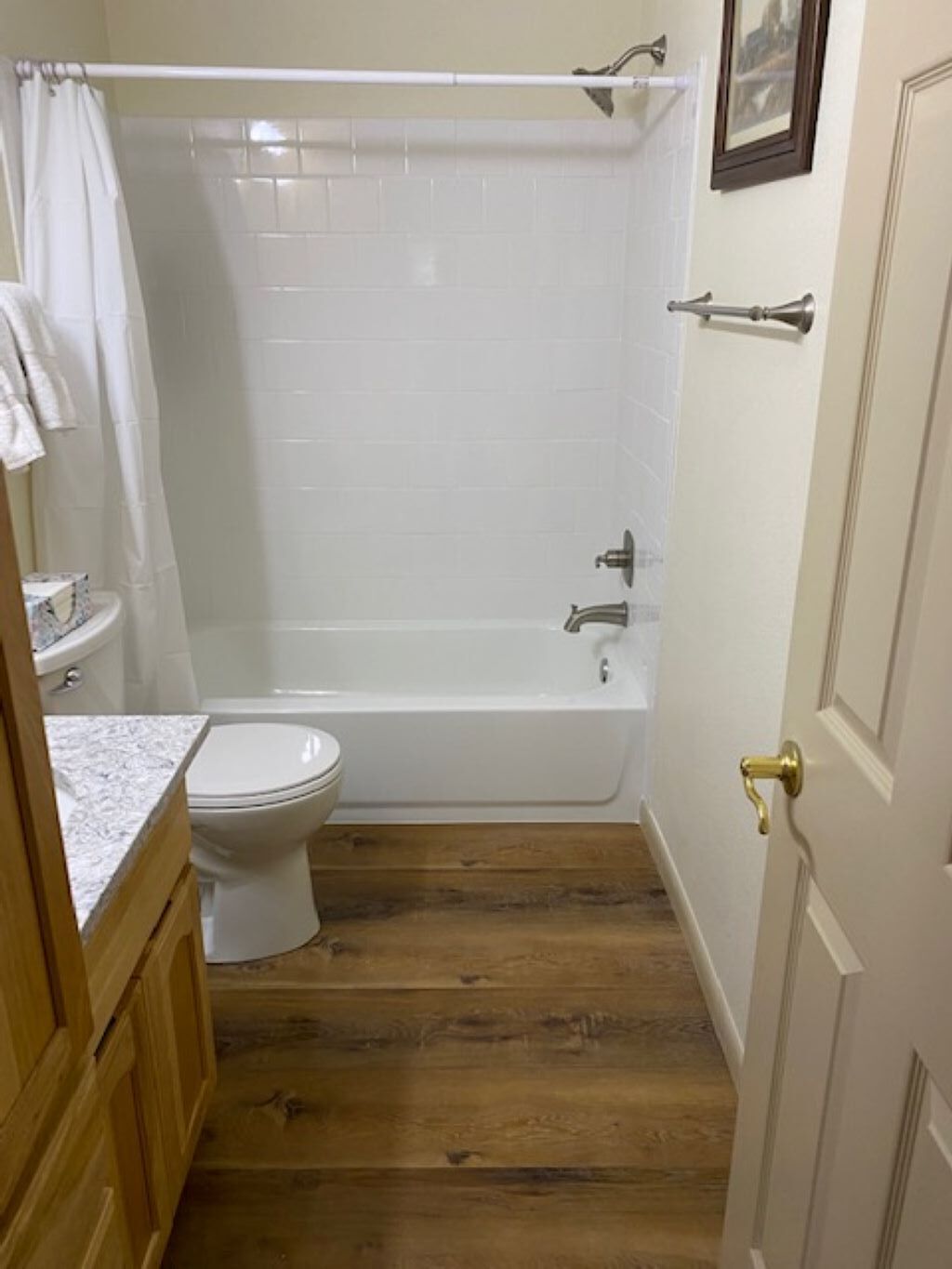 A bathroom with a toilet, bathtub, and wooden flooring.