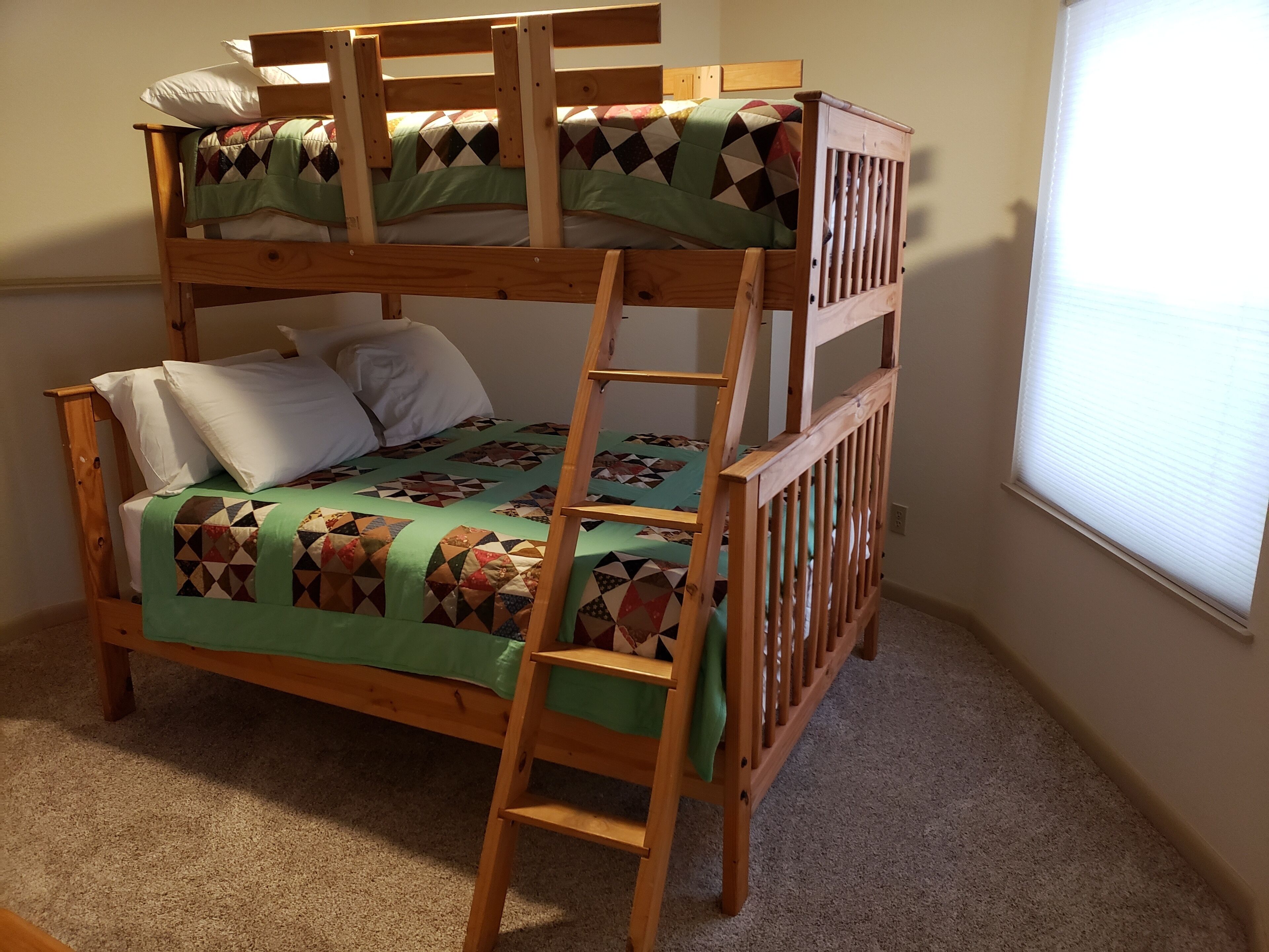 A bunk bed with a ladder, a green blanket, and pillows.