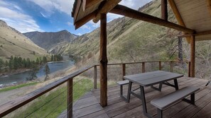 En træterrasse med et picnicbord og bænke med udsigt over en flod og bjerge.
