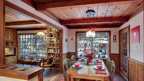 A dining area with a wooden table set for four, surrounded by chairs. There is a bookshelf filled with books and a window with a view of trees. - Murphys Getaway - Enjoy Wineries, Hiking, Concerts, Shopping & Small Town Charm (Murphys)