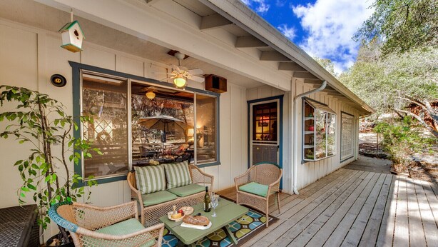 A covered porch with wicker furniture, a dining table with a bottle and bread, and a view of the backyard. - Murphys Getaway - Enjoy Wineries, Hiking, Concerts, Shopping & Small Town Charm (Murphys)