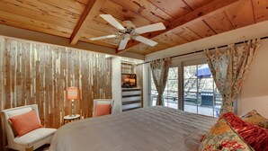 A bedroom with a large bed, a ceiling fan, wooden walls, a window with curtains, and a view of the outdoors. - Murphys Getaway - Enjoy Wineries, Hiking, Concerts, Shopping & Small Town Charm (Murphys)