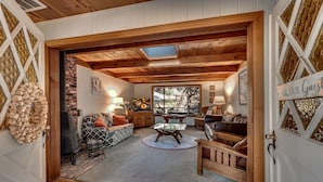 A cozy living room with a fireplace, wooden ceiling, and a large window. - Murphys Getaway - Enjoy Wineries, Hiking, Concerts, Shopping & Small Town Charm (Murphys)