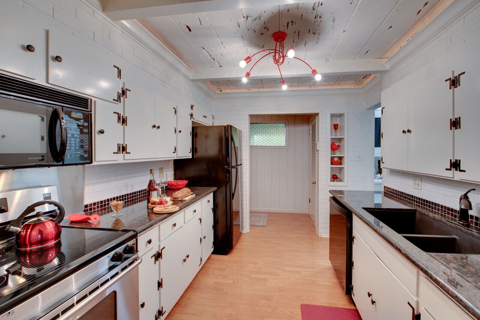 A modern kitchen with white cabinetry, stainless steel appliances, and a red pendant light.