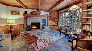 A cozy living room with a fireplace, wooden furniture, and a large window offering a view of the outdoors. - Murphys Getaway - Enjoy Wineries, Hiking, Concerts, Shopping & Small Town Charm (Murphys)