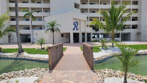 A multi-story hotel with a central entrance, palm trees, and a water feature. - Riviera Club 9th floor Direct Beach Front IAN UPDATED AND READY!!! (Fort Myers Beach)
