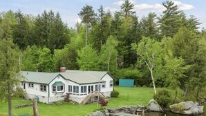 Ein Haus mit überdachter Veranda, einer Steinmauer und einem Steg, der in einen Teich führt.