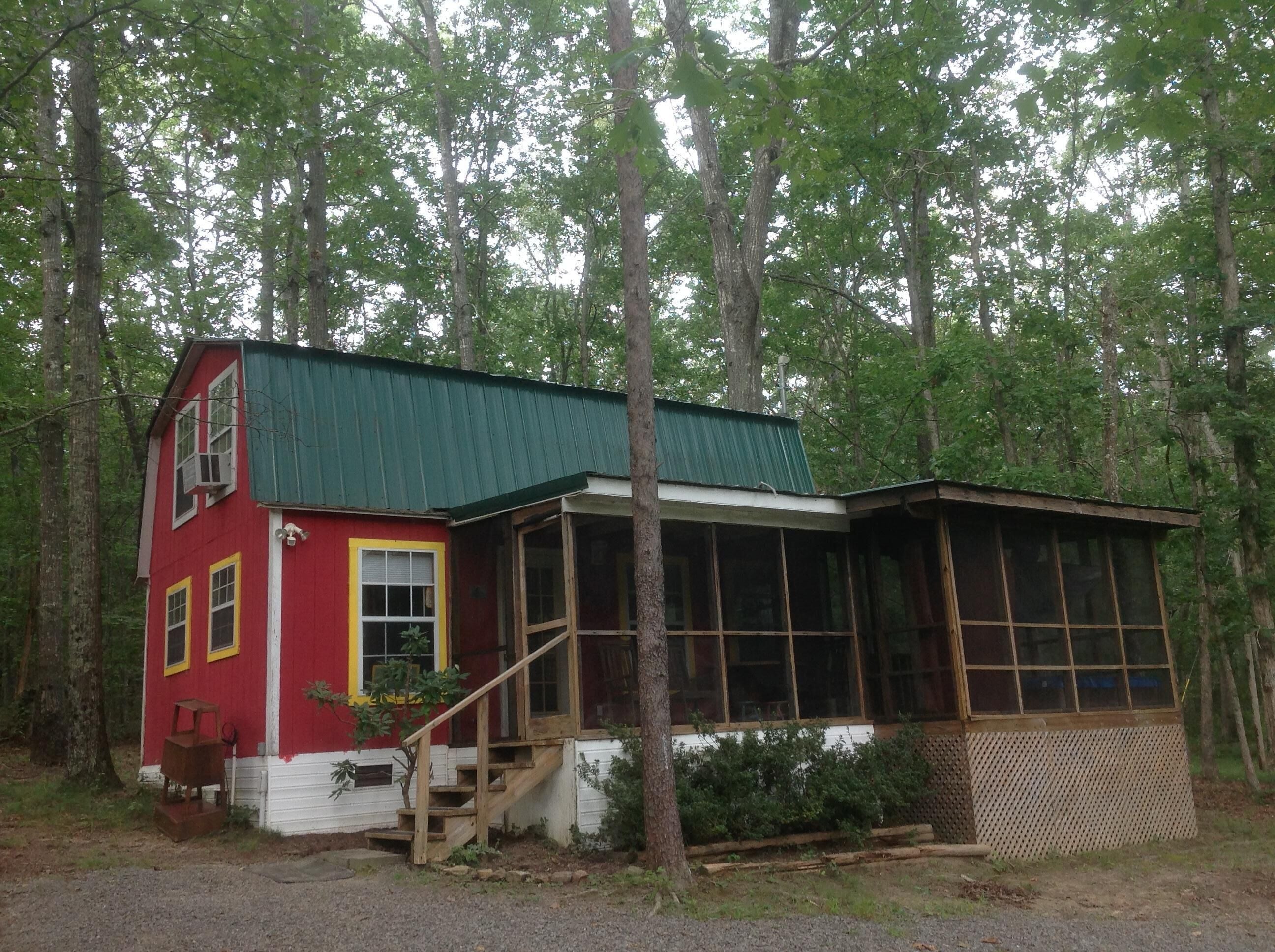 A two-story cabin with a green roof, surrounded by trees.