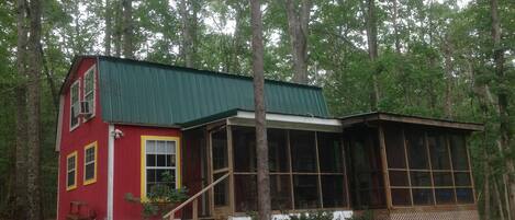 A two-story cabin with a green roof, surrounded by trees.