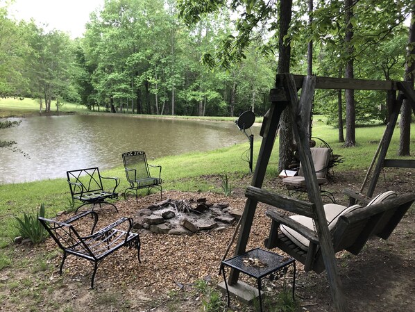 A lakeside patio with metal chairs, a fire pit, and a swing set. - Black Bear (Mentone)