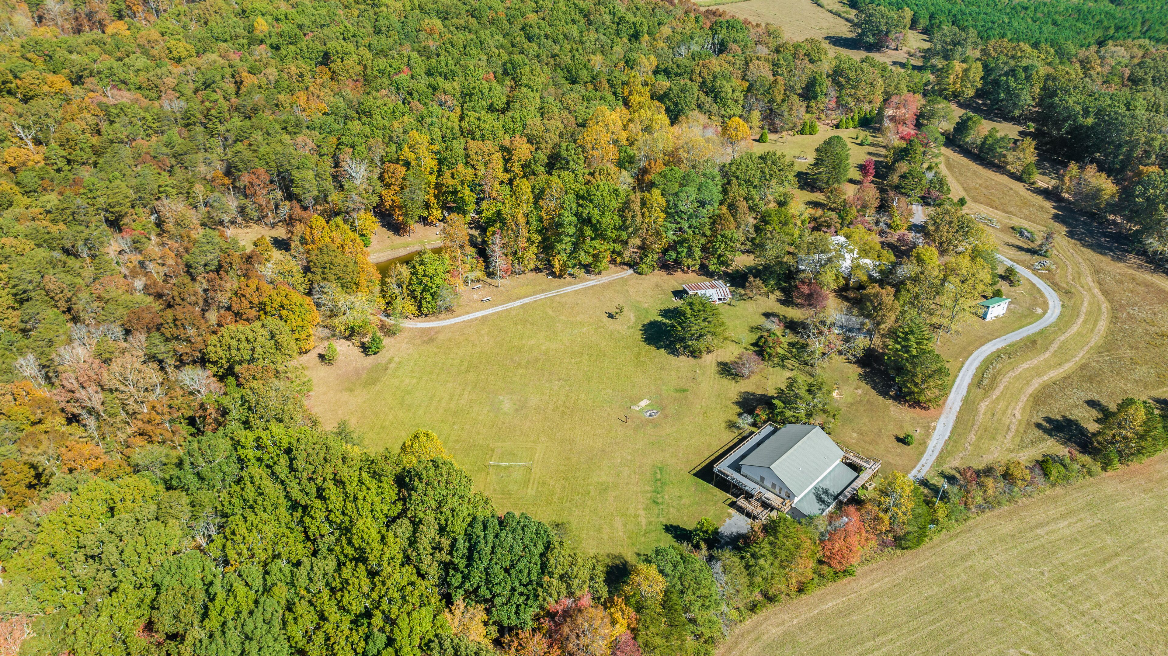An aerial view of a property with a large grassy field, a winding road, and a house with a sloped roof.
