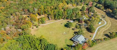 An aerial view of a property with a large grassy field, a winding road, and a house with a sloped roof.