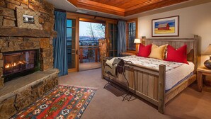 A bedroom with a stone fireplace, a bed with red and beige pillows, a colorful rug, and a painting on the wall. - Teton Village Ski-In Ski-Out Crystal Springs Luxury Condominium Jackson Hole WY (Teton Village)