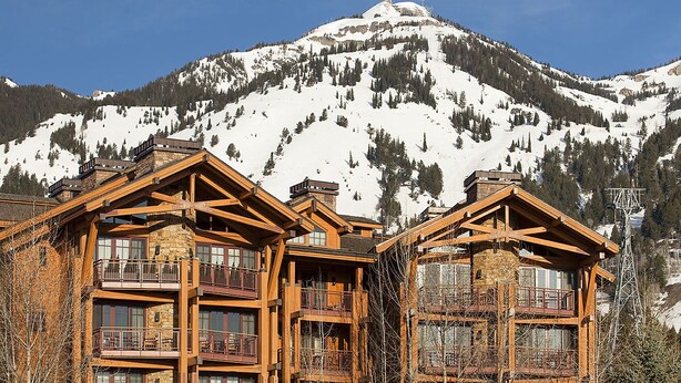 Una cabaña de varios pisos con balcones, con una imponente montaña nevada de fondo.