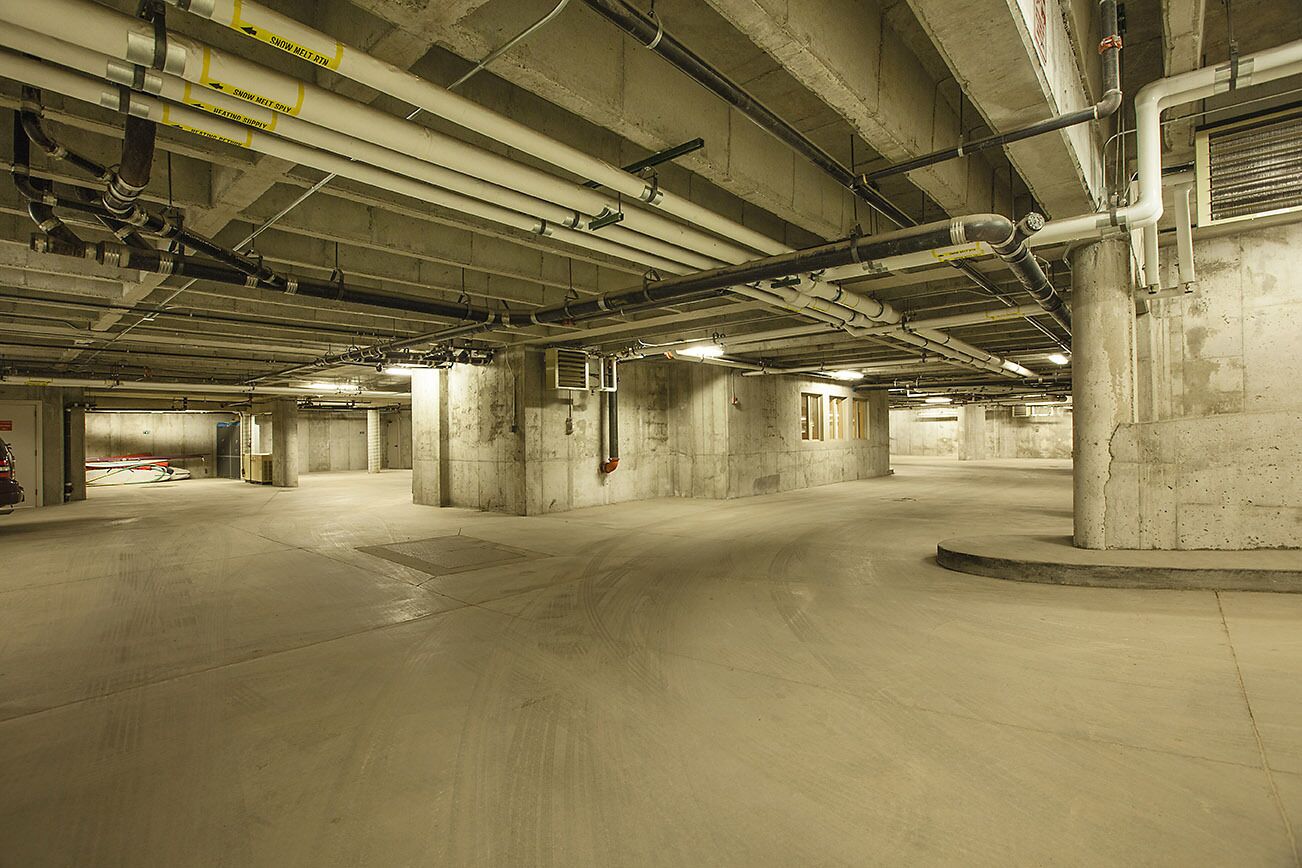 A spacious underground parking garage with concrete pillars and overhead pipes.