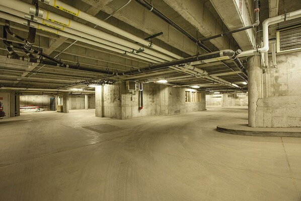A spacious underground parking garage with concrete pillars and overhead pipes.