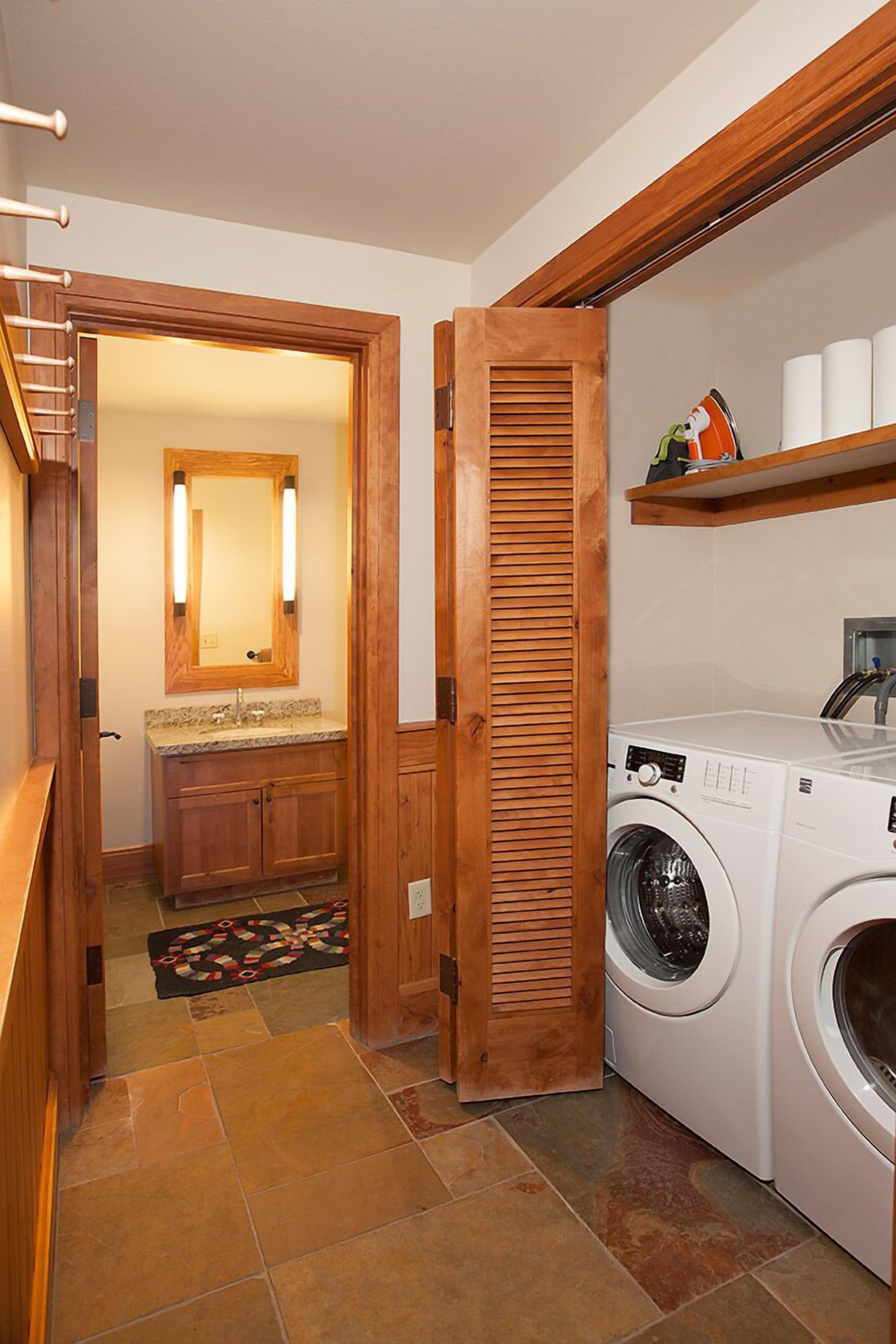 A laundry room with a washing machine, a wooden door, a mirror, and a shelf with towels.