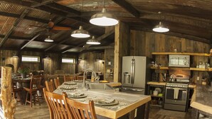 Une cuisine rustique aux murs en bois, avec un îlot central doté de chaises, un réfrigérateur, un four et un évier.