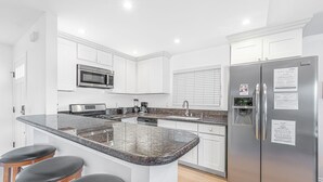 A modern kitchen with white cabinets, a granite countertop, a stainless steel refrigerator, and a built-in microwave.