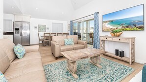 A spacious living area with a beige sofa, a wooden coffee table, and a large window offering a view of the ocean.
