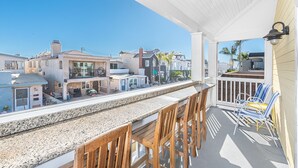 A balcony with a granite countertop, wooden chairs, and a view of neighboring houses.