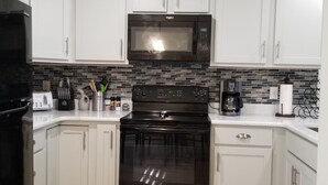 A kitchen with white cabinets, a black microwave, a black stove, and a black refrigerator. - Welcome to your affordable beach vacation (Gulf Shores)