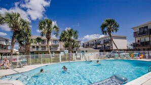 A swimming pool surrounded by palm trees and a multi-story building with balconies. - Welcome to your affordable beach vacation (Gulf Shores)