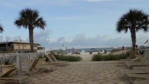A beachside patio with lounge chairs, palm trees, and a view of the beach and ocean. - Welcome to your affordable beach vacation (Gulf Shores)