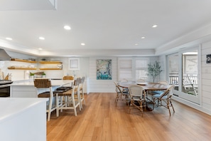 Una cocina moderna con armarios blancos, piso de madera y un comedor con sillas de mimbre y una mesa de madera.