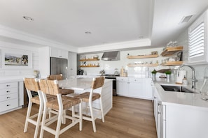 Una cocina moderna con armarios blancos, una isla central con sillas y suelo de madera.