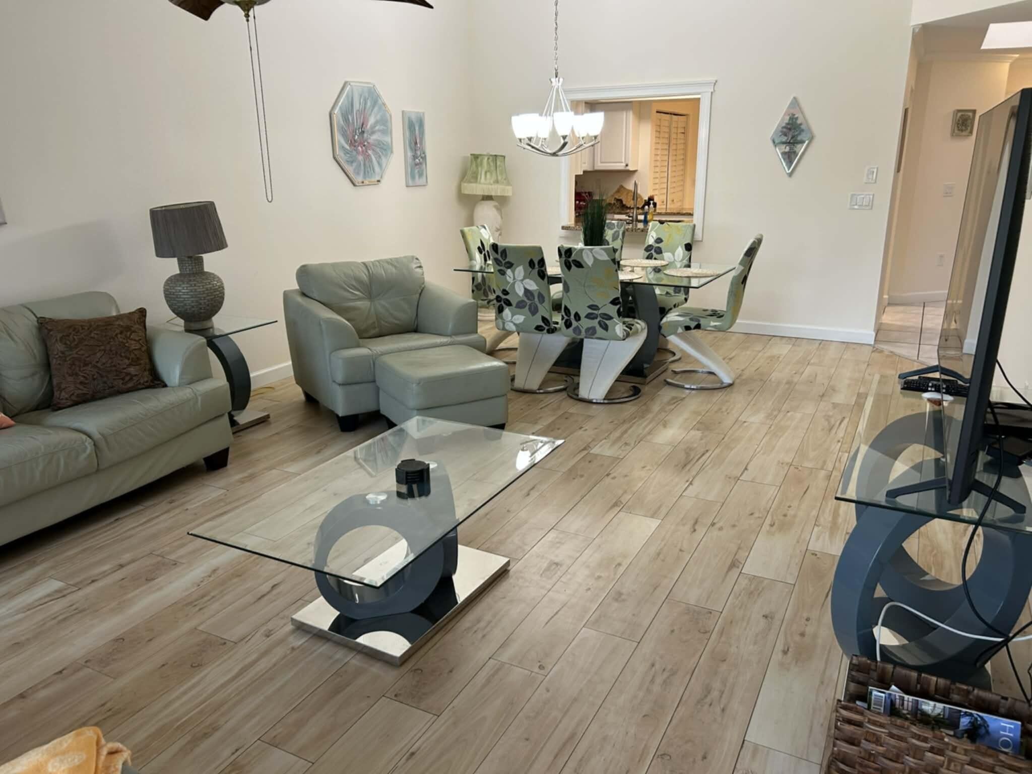 A modern living room with a glass coffee table, a sofa, a dining table with chairs, and a kitchen in the background.