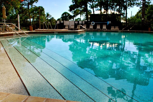 A clear swimming pool with a tiled edge, surrounded by lounge chairs and a fence.