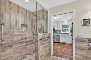Un baño moderno con cabina de ducha de vidrio, un pasamanos y suelo de baldosas.