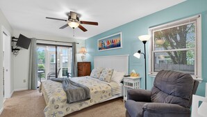 A bedroom with a bed, a chair, a ceiling fan, a painting, and a window with blinds.