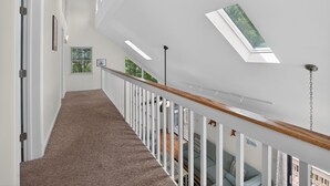 A modern interior with a carpeted hallway, white walls, a wooden railing, and a skylight.